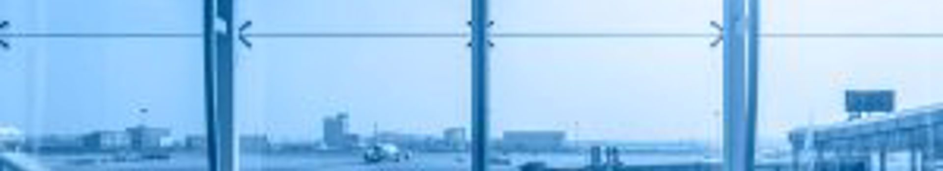 Photo of an airport window with an airplane taking off in the backgrond